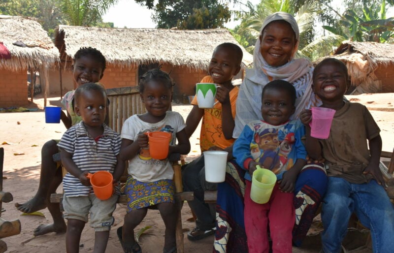 A woman and a group of children holding water cups, smiling.