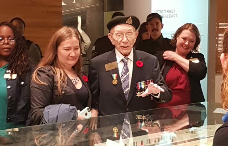 Un ancien combattant et sa petite-fille se tiennent devant une vitrine contenant la maquette du hangar d’immigration du Quai 21.