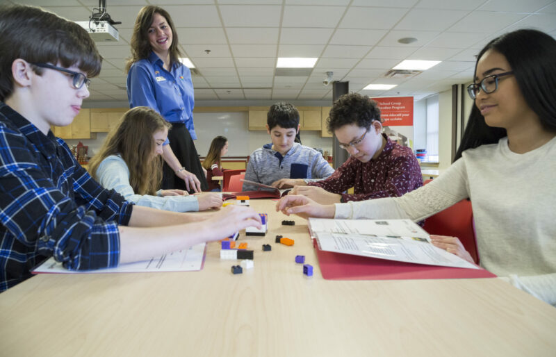 Des élèves sont assis face à face à une table dans la salle de classe du Musée, tandis qu’un interprète du patrimoine les guide à travers l’un des programmes éducatifs utilisant des blocs Lego.