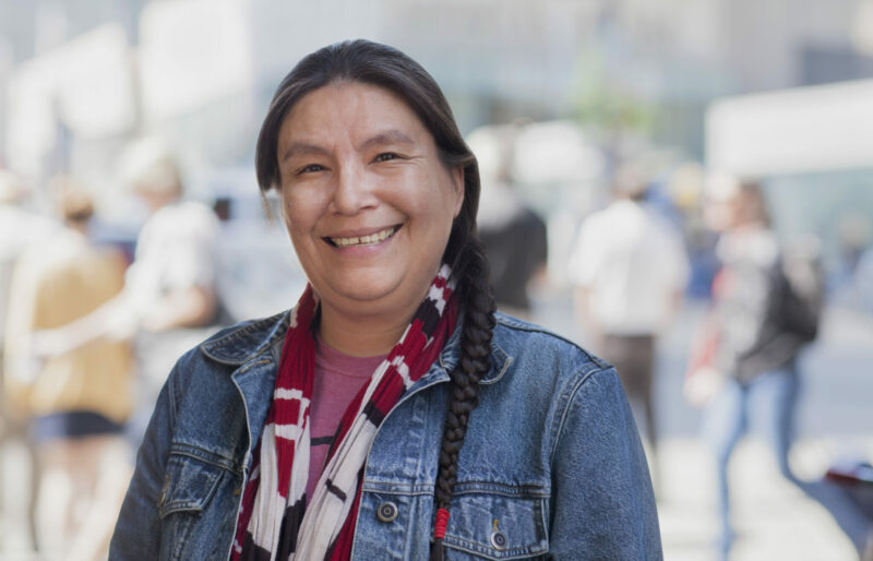 Une femme des Premières nations en veste en jean sourit à la caméra smiles for the camera