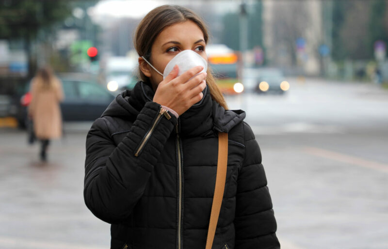 Une jeune femme portant un masque facial marche dans une rue de la ville.