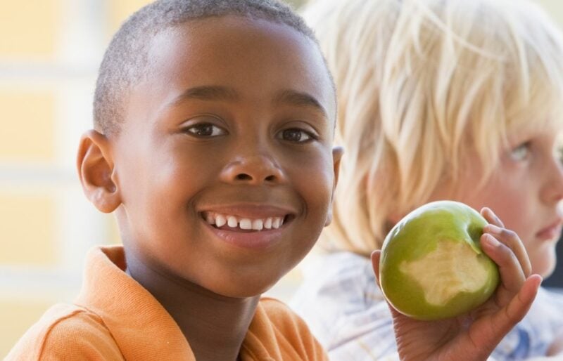 Jeune garçon noir mangeant une pomme verte avec quelques bouchées.