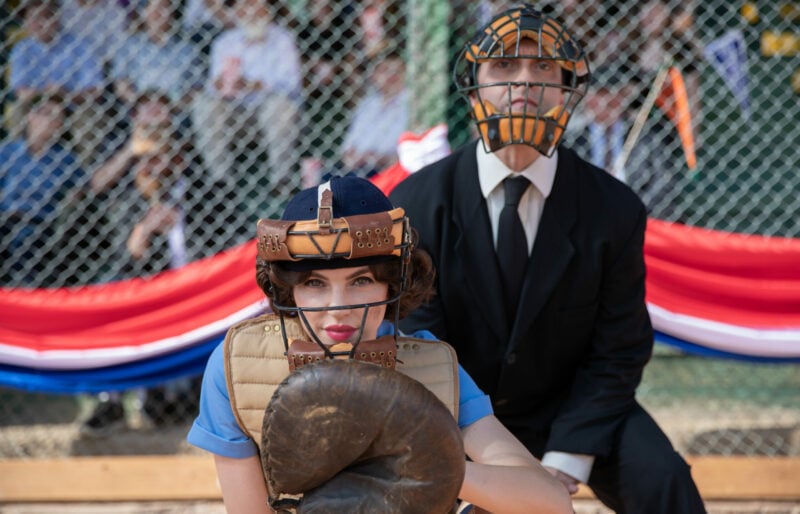 Une receveuse de baseball s'accroupit devant un arbitre pendant un match.