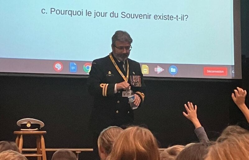 Un officier en uniforme devant un écran s'adresse à un auditoire d'étudiants.