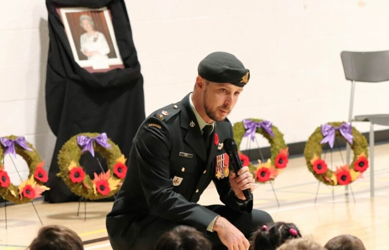Un officier militaire en uniforme parle dans un microphone tout en s'adressant à un gymnase d'enfants.